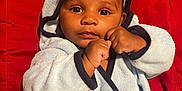 Kingston is registered to the contest to win money with this photo: baby, child, infant, face, eyes, hands, hood, robe, clothing, fist, cute, portrait, red_background, smiling, skin, person, sitting, indoor, young, expression