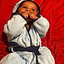 Kingston joined the competition — help win amazing prizes! baby, child, robe, blue_robe, red_background, sucking_fist, infant, cute, cozy, portrait, indoors, young_child, expression, hands, face, curious, soft_texture, clothing, lying_down, adorable