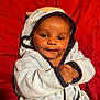 baby, child, hooded_robe, blue_clothing, smiling, dimples, face, hands, red_background, cozy, cute, infant, portrait, warmth, soft_lighting, indoors, person, young_child, happy, apparel