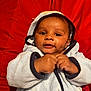 Kingston is registered to the contest to win money with this photo: baby, infant, child, hooded_towel, red_background, cute, smiling, hands, face, portrait, cozy, soft_texture, clothing, lying_down, indoor, young_child, skin, eyes, expression, cute_face