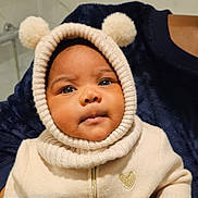 Théa participe au concours pour gagner de l'argent avec cette photo : baby, child, face, hood, knit, pom_poms, cream_color, gold_heart, clothing, portrait, cute, warm, indoor, person, infant, closeup, expression, soft_texture, sweater, adorable