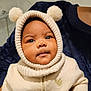 baby, child, face, hood, knit, pom_poms, cream_color, gold_heart, clothing, portrait, cute, warm, indoor, person, infant, closeup, expression, soft_texture, sweater, adorable