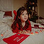 child, girl, bed, red_sweater, string_lights, christmas_letter, holiday_decor, christmas_tree, indoor, cozy, smiling, long_hair, bedspread, festive, warm_lighting, portrait, holiday, cute, happy, home