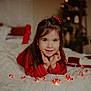 child, girl, smile, red_sweater, hands, face, string_lights, candy_cane, blanket, bed, holiday, christmas_tree, decor, cozy, indoors, portrait, cute, happy, warm, soft_focus