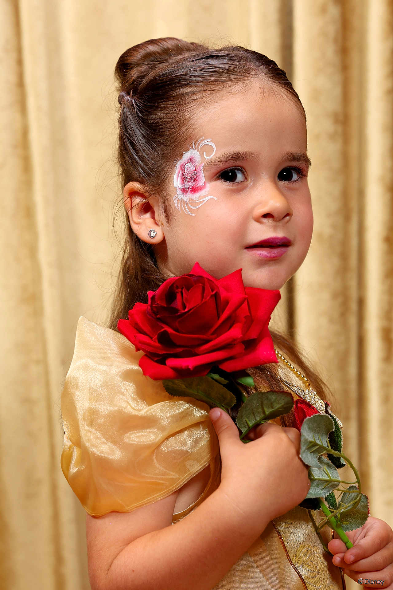 Alyssa a rejoint le concours — aidez-le/la à gagner de superbes lots ! child, girl, face_paint, rose, flower, dress, costume, portrait, close_up, earrings, hair, brown_hair, hand, skin, young, indoor, golden_background, holding, red_rose, smiling