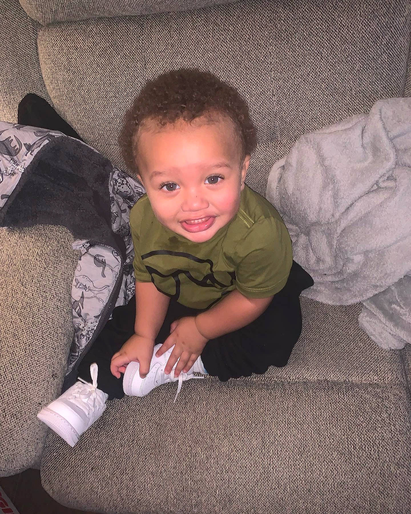 Landyn is registered to the contest to win money with this photo: baby, baby_toddler_clothing, carmine, cheek, child, comfort, couch, floor, flooring, hardwood, human_body, human_leg, joy, lap, linens, person, room, sitting, sleeve, smile