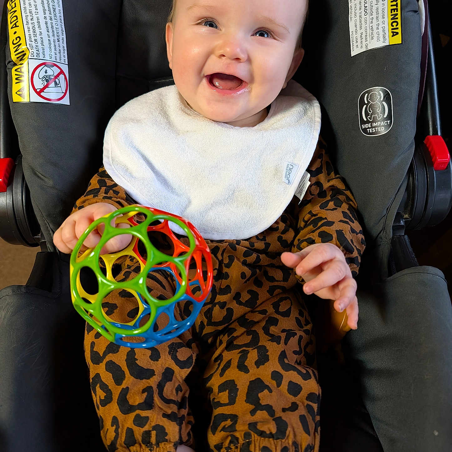 Sophia joined the competition — help win amazing prizes! baby, infant, smiling, car_seat, bib, toy, leopard_print, clothing, happy, child, face, hand, footwear, indoor, seat, colorful, plastic, play, person, young