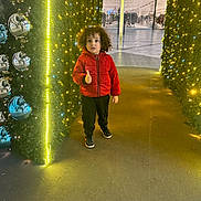 Nidhal participe au concours pour gagner de l'argent avec cette photo : child, curly_hair, red_jacket, thumbs_up, festive_lights, yellow_lights, silver_ornaments, tunnel, indoor, shopping_mall, floor, casual_clothing, black_pants, sneakers, holiday_decor, smiling, person, photography, modern, reflection