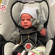 Enzo joined the competition — help win amazing prizes! baby, newborn, car_seat, infant, mittens, hat, striped_pants, feet, straps, safety, child, person, indoors, cute, expression, seat, fabric, cushion, warning_label, closeup
