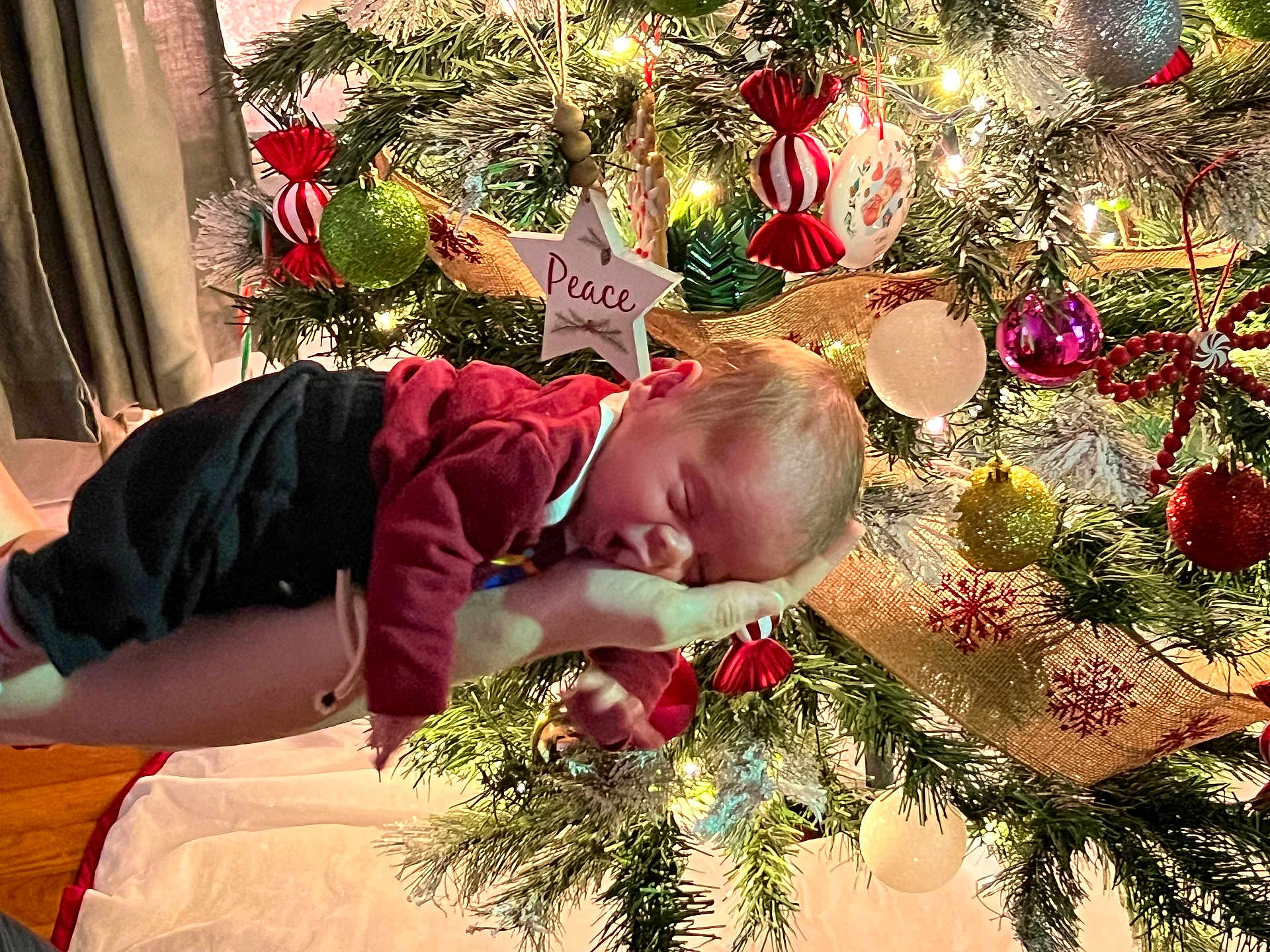 Enzo joined the competition — help win amazing prizes! baby, newborn, sleeping, hand, christmas_tree, ornaments, lights, holiday, festive, red_clothing, greenery, decorations, peace_star, background, indoor, soft_lighting, cozy, person, celebration, winter