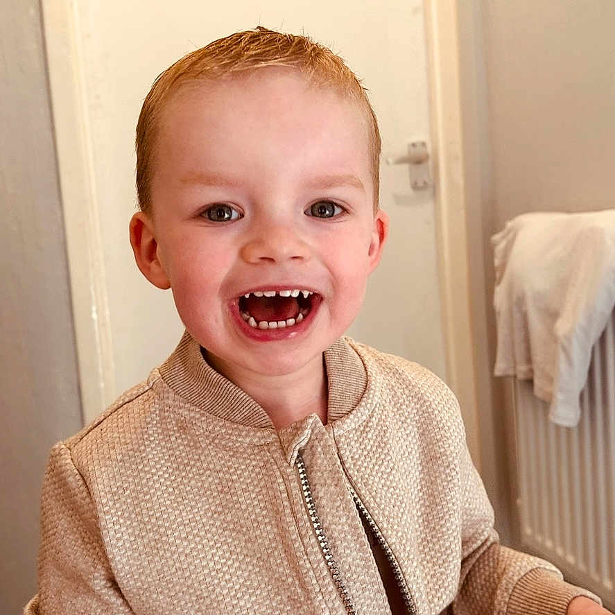 Oliver is registered to the contest to win money with this photo: beige, child, clothing, cute, door, expression, face, happy, indoor, jacket, light_skin, person, portrait, radiator, short_hair, smiling, standing, teeth, towel, young