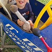 Ethan participe au concours pour gagner de l'argent avec cette photo : child, boy, smiling, plush_toy, dinosaur_toy, pedal_car, blue_car, yellow_steering_wheel, grass, outdoor, people_legs, casual_clothing, happy, toy, playtime, daylight, seat, footwear, fun, cute