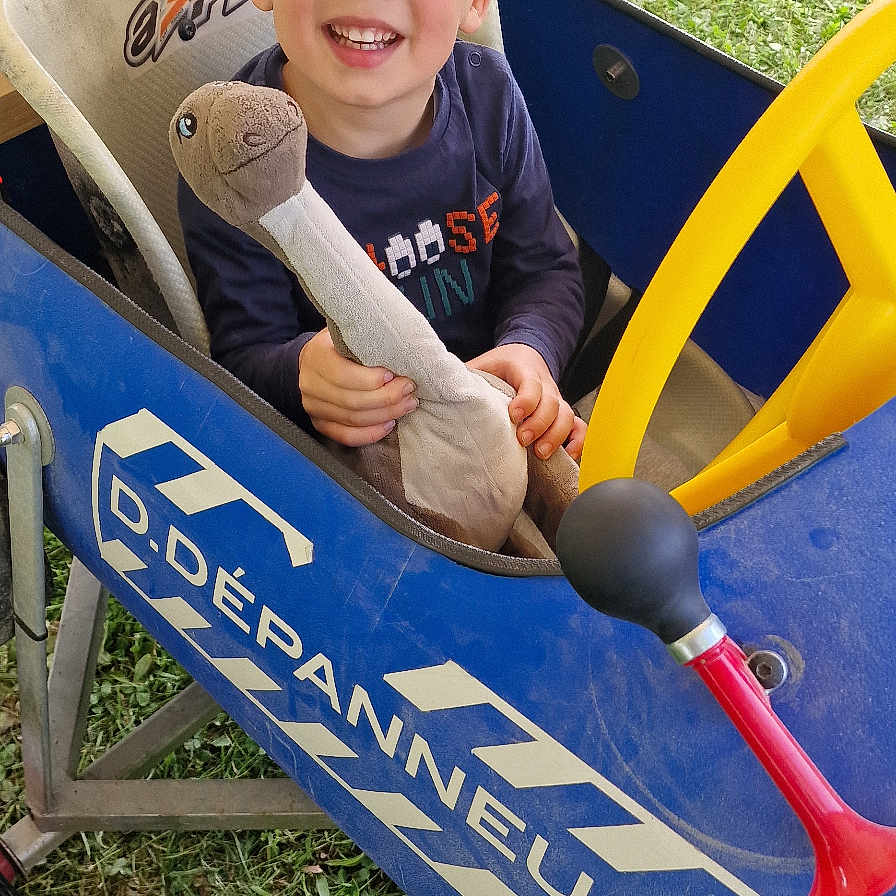 Ethan participe au concours pour gagner de l'argent avec cette photo : blue_car, boy, casual_clothing, child, cute, daylight, dinosaur_toy, footwear, fun, grass, happy, outdoor, pedal_car, people_legs, playtime, plush_toy, seat, smiling, toy, yellow_steering_wheel
