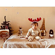 Nolann a rejoint le concours — aidez-le/la à gagner de superbes lots ! toddler, child, reindeer_antlers, christmas_tree, plush_toy, gnome, blanket, holiday, decorations, indoor, cozy, beige, sitting, cute, festive, winter, smiling, face, toy, holiday_season