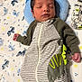 baby, newborn, sleeping, infant, onesie, striped_clothing, dinosaur_design, blanket, pillow, patterned_blanket, cozy, peaceful, resting, child, indoor, soft_texture, cute, person, hand, head