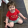 toddler, child, smiling, curly_hair, red_shirt, shorts, sitting, floor, tile, white_sneakers, feet, indoor, happy, person, casual, playful, cute, young, portrait, home