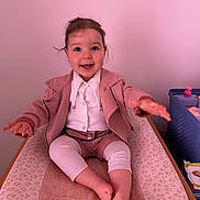 Mia a rejoint le concours — aidez-le/la à gagner de superbes lots ! baby_supplies, barefoot, basket, changing_pad, child, cute, face, furniture, happy, indoor, leggings, person, pink_jacket, reaching, room, sitting, smiling, toddler, white_shirt, young_child