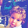 cabinet, candid, child, clock, curly_hair, cute, face, floor, floral_shirt, furniture, home, indoor, person, portrait, smile, soft_light, technology, toddler, tv, young_child