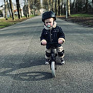 Elio a rejoint le concours — aidez-le/la à gagner de superbes lots ! balance_bike, casual_clothing, child, daytime, helmet, jacket, knee_pads, outdoor, pacifier, park, person, protective_gear, road, safety, shoes, sidewalk, street, toddler, trees, young_child
