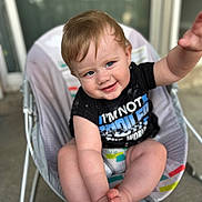 Skyler is registered to the contest to win money with this photo: baby, child, infant, blue_eyes, smiling, black_shirt, sitting, baby_seat, curly_hair, cute, playful, reaching_hand, indoor, colorful, legs_crossed, happy, portrait, young_child, chubby_cheeks, diaper