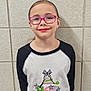 casual, child, cute, eyewear, face, fashion, girl, glasses, graphic_tshirt, happy, indoor, long_sleeve_shirt, person, pink_glasses, portrait, smile, standing, tiled_wall, wall, youth
