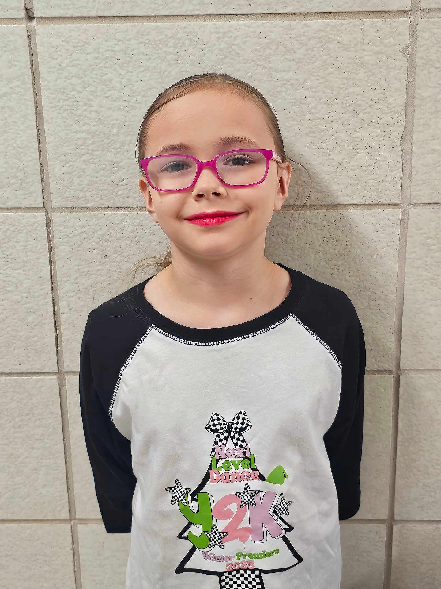 Melodee is registered to the contest to win money with this photo: casual, child, cute, eyewear, face, fashion, girl, glasses, graphic_tshirt, happy, indoor, long_sleeve_shirt, person, pink_glasses, portrait, smile, standing, tiled_wall, wall, youth