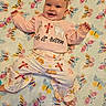 baby, child, smiling, blanket, butterfly_pattern, pink_clothing, headband, cross, lamb, bunny, happy, infant, cute, laying_down, patterned_pants, soft_texture, indoors, portrait, cheerful, baby_clothes