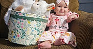 Maesyn is registered to the contest to win money with this photo: baby, child, plush_toys, stuffed_animals, basket, couch, curtain, headband, pink_clothing, smiling, indoor, decor, patterned_fabric, footwearless, happy, seated, toy, person, infant, living_room