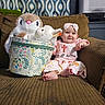 baby, child, plush_toys, stuffed_animals, basket, couch, curtain, headband, pink_clothing, smiling, indoor, decor, patterned_fabric, footwearless, happy, seated, toy, person, infant, living_room