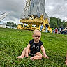 Maesyn is registered to the contest to win money with this photo: baby, grass, rocket, people, cloudy_sky, outdoor, child, onesie, greenery, technology, tourists, park, curious, serious_expression, daylight, nature, structure, large_object, sitting, casual_clothing