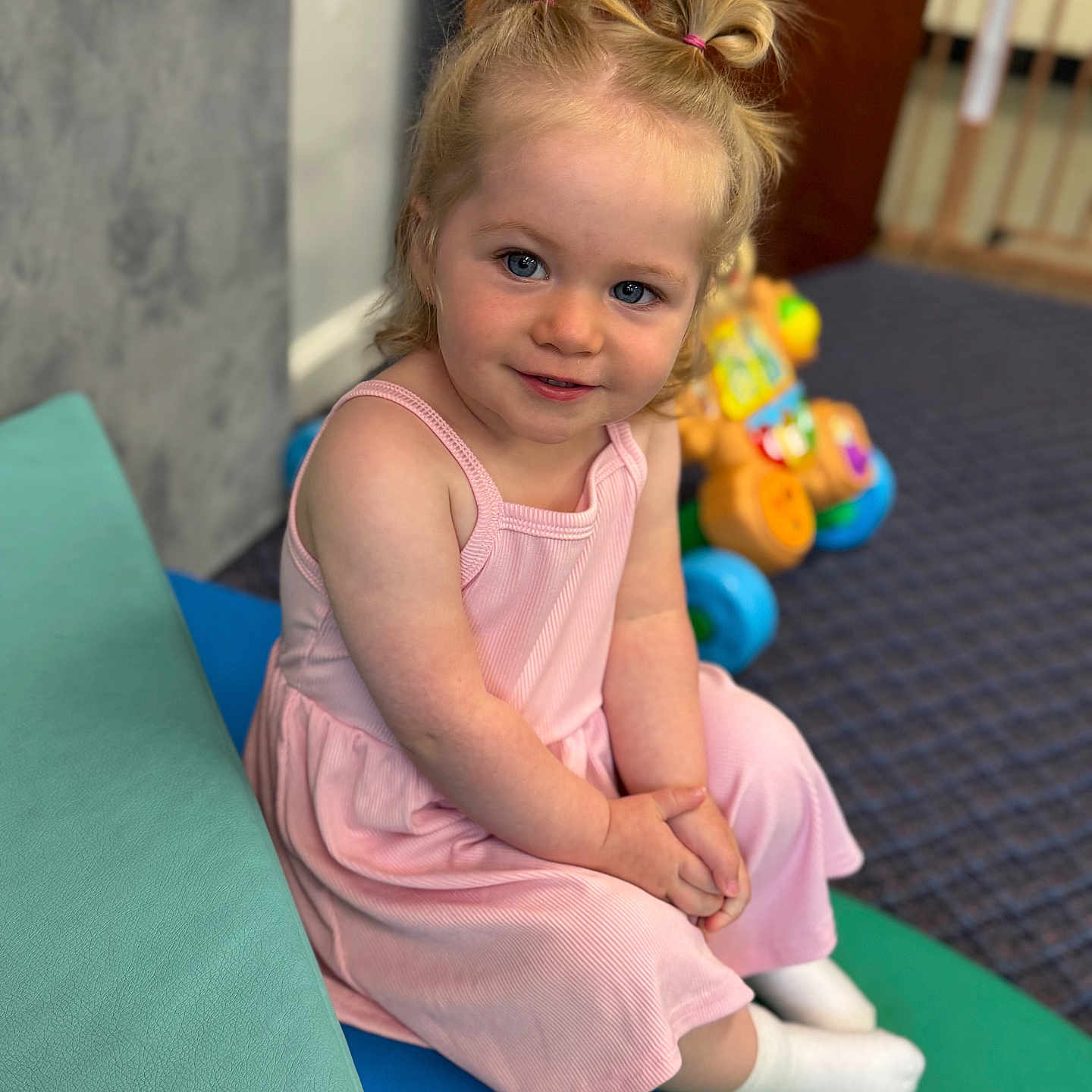 Amelia is registered to the contest to win money with this photo: blue_eyes, carpet, casual_clothing, child, cushions, cute, girl, hair_ties, happy, indoor, pink_dress, playroom, portrait, sitting, smile, toddler, toy, white_socks, wooden_door, young_child
