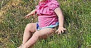 Olivia is registered to the contest to win money with this photo: child, grass, outdoor, nature, sitting, pink_clothing, sandals, young_child, sunlight, greenery, casual, playful, summer, portrait, person, legs, face, blond_hair, daytime, hill