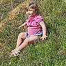 blond_hair, casual, child, daytime, face, grass, greenery, hill, legs, nature, outdoor, person, pink_clothing, playful, portrait, sandals, sitting, summer, sunlight, young_child