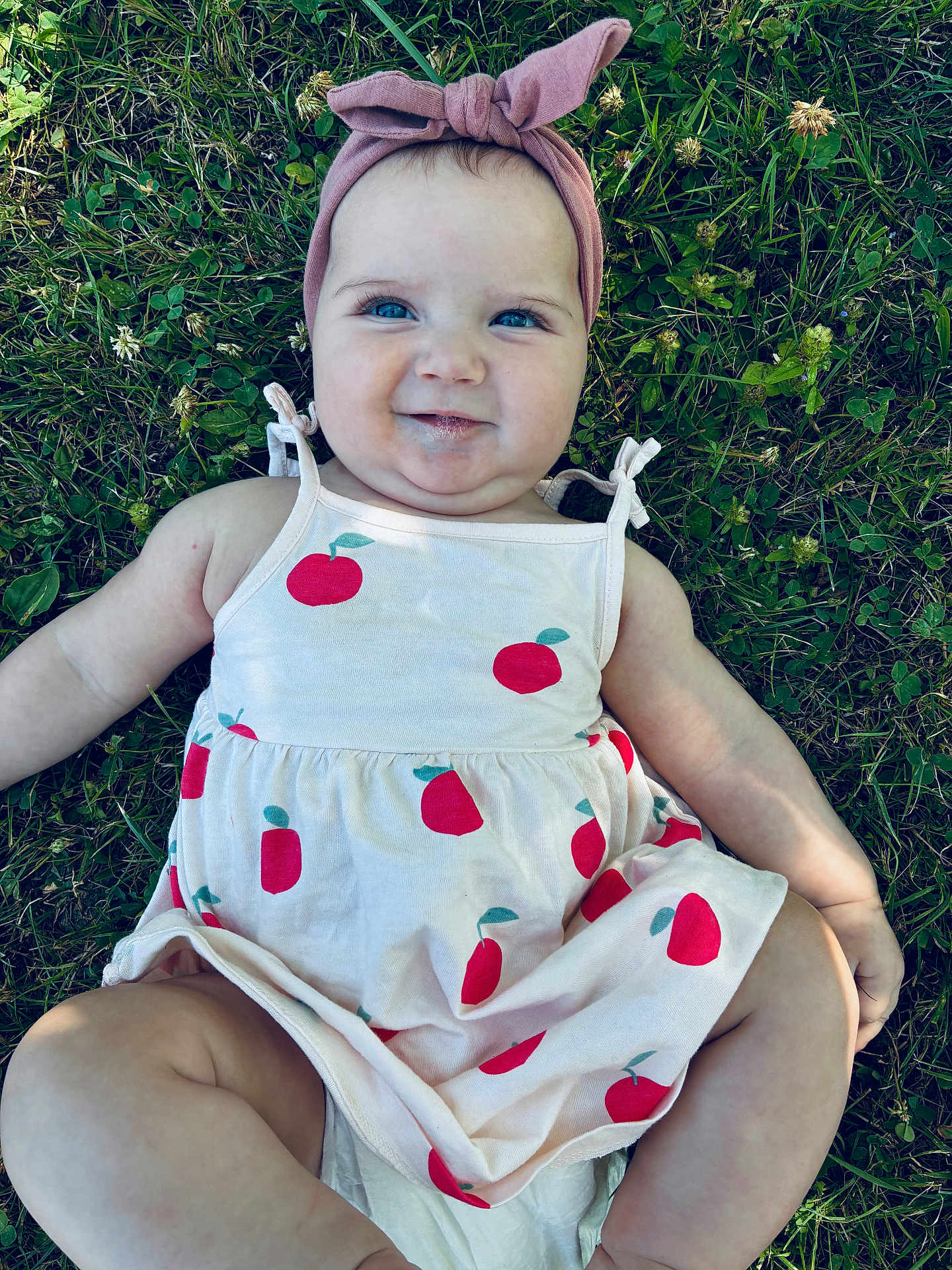 Leya participe au concours pour gagner de l'argent avec cette photo : baby, child, grass, headband, dress, apple_print, smile, blue_eyes, outdoor, greenery, clover, drool, cute, lying_down, summer, nature, skin, person, infant, playful