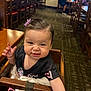black_shirt, blanket, carpet, child, cute, dining, funny_face, furniture, hair_clip, high_chair, indoor, people, person, purple_flower, reaching_hand, restaurant, smiling, table, toddler, wooden_chair