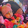 baby, pink_hat, pom_poms, car_seat, toy, colorful_toy, pink_sweater, blanket, indoor, child, cute, sparkles, hearts, playful, infant, seated, warm_clothing, focus, adorable, cozy
