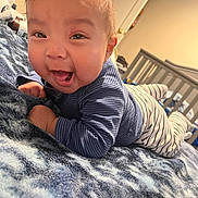 Yael joined the competition — help win amazing prizes! baby, infant, smiling, blue_clothing, striped_pants, blanket, bedroom, crib, indoor, happy, face, person, child, toddler, cute, young, lying_down, cozy, soft_texture, home