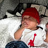 baby, sleeping, red_hat, white_onesie, blanket, blue_blanket, stroller, infant, cozy, peaceful, child, portrait, soft_texture, clothing, resting, cute, indoors, young_child, headwear, baby_garment