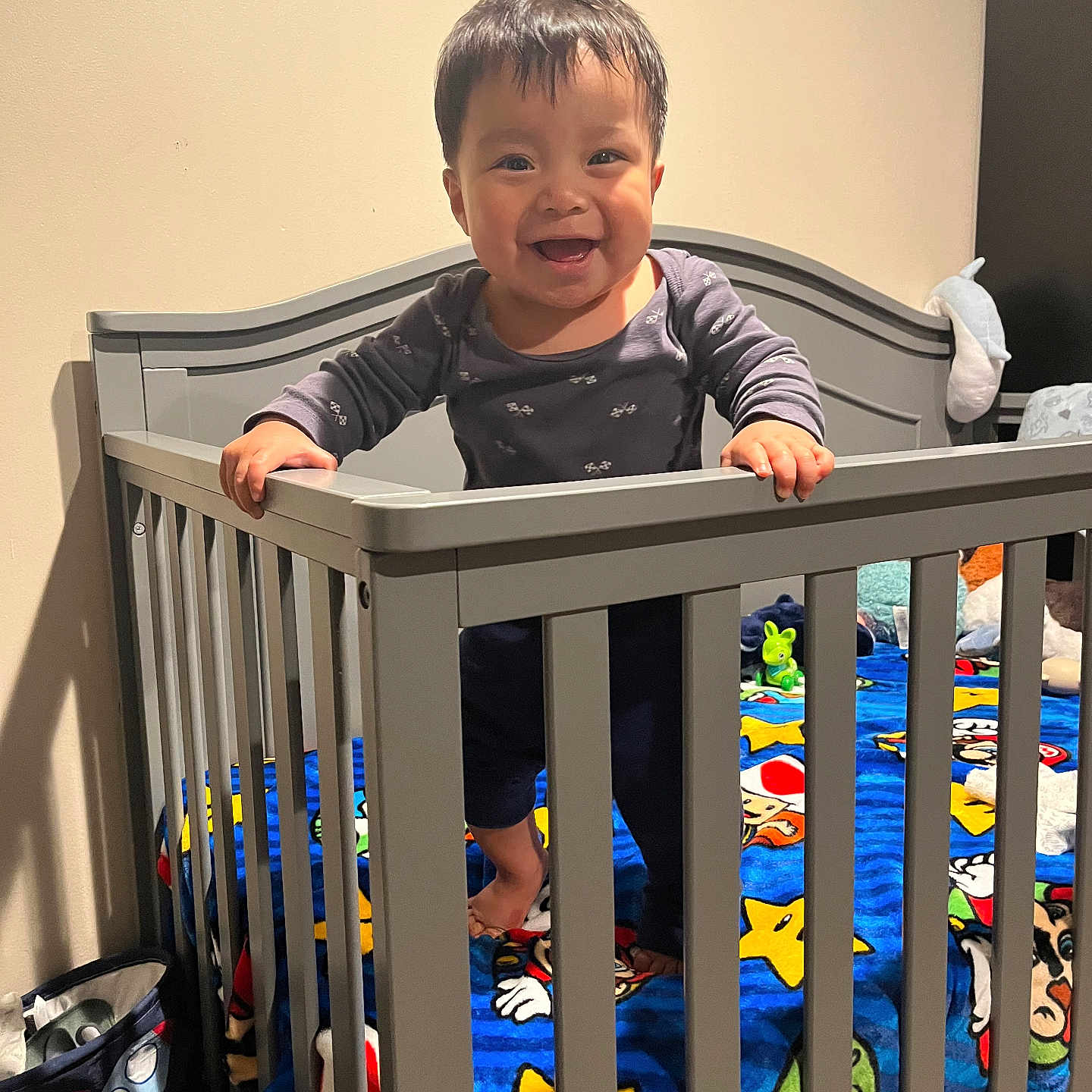 Yael is registered to the contest to win money with this photo: baby, bedding, bedroom, blanket, cartoon, child, colorful, crib, dark_hair, family, happy, home, indoor, infant, nursery, portrait, railing, smiling, standing, toy