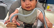 Yael joined the competition — help win amazing prizes! baby, bibs, blue_toy, child, couch, curtains, face, furniture, happy, high_chair, indoor, infant, living_room, person, play, seat, smiling, toy, window, wooden_rings