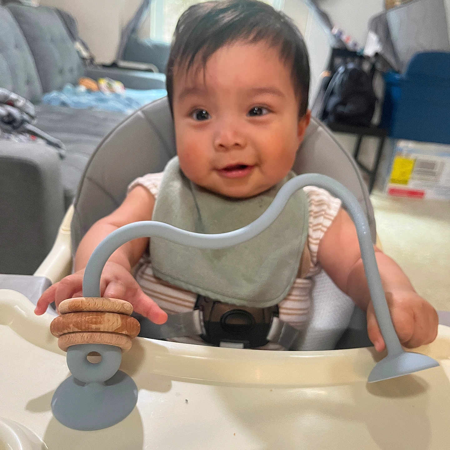 Yael joined the competition — help win amazing prizes! baby, bibs, blue_toy, child, couch, curtains, face, furniture, happy, high_chair, indoor, infant, living_room, person, play, seat, smiling, toy, window, wooden_rings