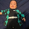 baby, baby_boy, baby_girl, black_clothing, casual, child, clothing, cute, dark_background, face, green_clothing, happy, indoor, infant, lying_down, one_person, patterned_clothing, portrait, smile, young_child