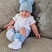 Enzo joined the competition — help win amazing prizes! baby, child, hat, pom_pom, socks, shoes, couch, pillow, knitwear, white_shoes, blue_hat, smiling, cute, indoor, portrait, sitting, cozy, fashion, infant, plush