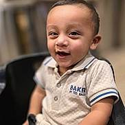 Hamza joined the competition — help win amazing prizes! baby, background_blur, beige_clothing, black_chair, casual_clothing, child, cute, expression, face, happy, indoor, person, polo_shirt, portrait, seated, short_hair, sitting, smiling, toddler, young_child