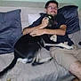 Eylau a rejoint le concours — aidez-le/la à gagner de superbes lots ! affection, black_dog, casual, couch, dog, domestic_animal, fur, glasses, happy, home, hugging, indoor, living_room, man, pet, pillows, relaxing, shorts, smiling, tail