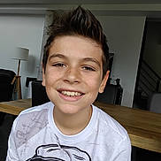 Louka participe au concours pour gagner de l'argent avec cette photo : boy, child, smiling, freckles, indoor, table, wood, lamp, hair, white_shirt, face, person, portrait, happy, casual, young, home, furniture, background, seated