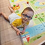 animal_print, baby, child, colorful, crawling, cute, floor, floor_tiles, fun, glasses, happy, indoor, play_mat, playtime, smile, toddler, toy, white_shorts, yellow_shirt, young_child