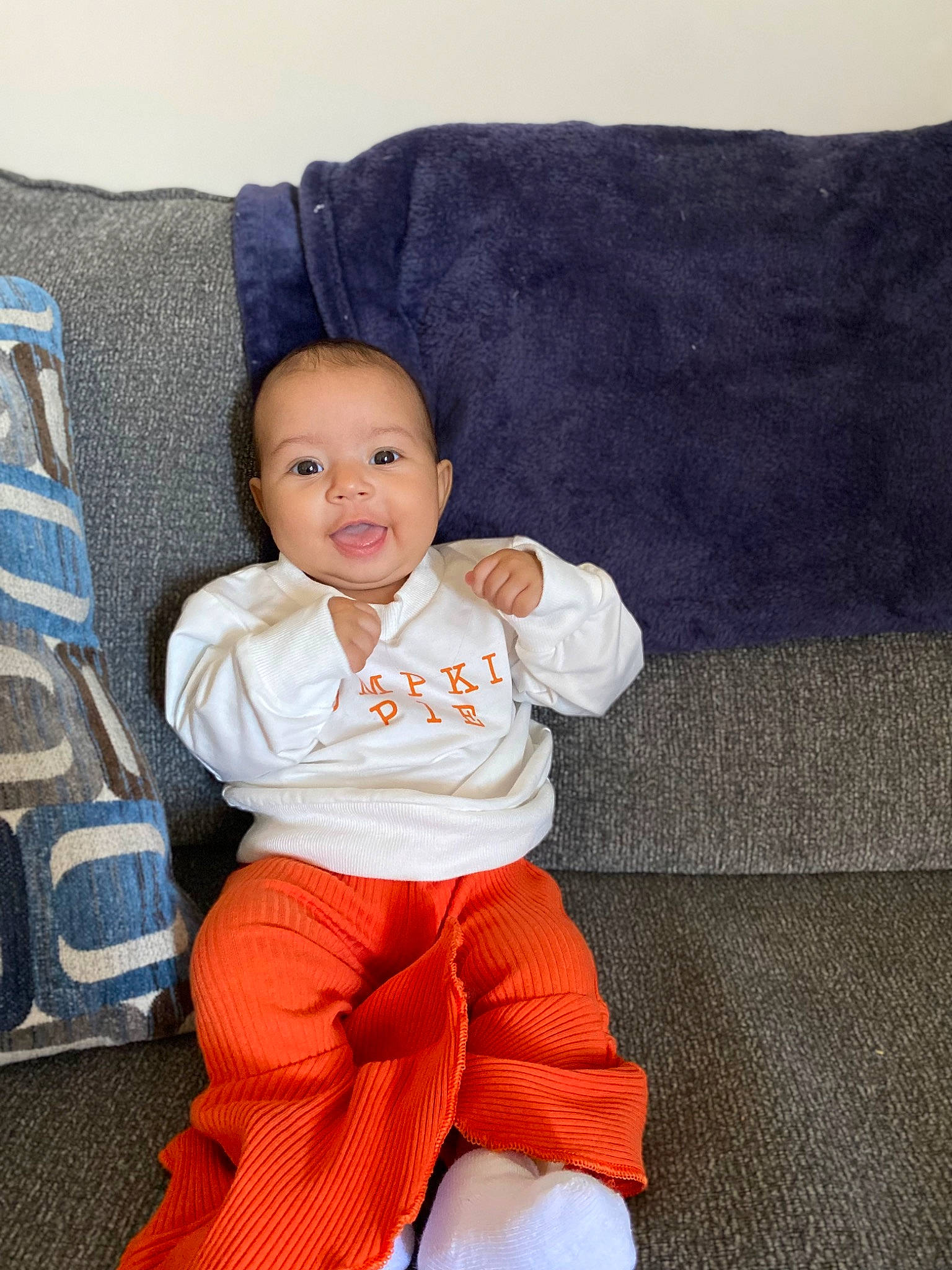 Esmé is registered to the contest to win money with this photo: baby, baby_toddler_clothing, comfort, couch, electric_blue, eye, face, fun, happy, head, human_leg, knee, linens, person, pillow, sitting, sleeve, smile, sportswear, t_shirt