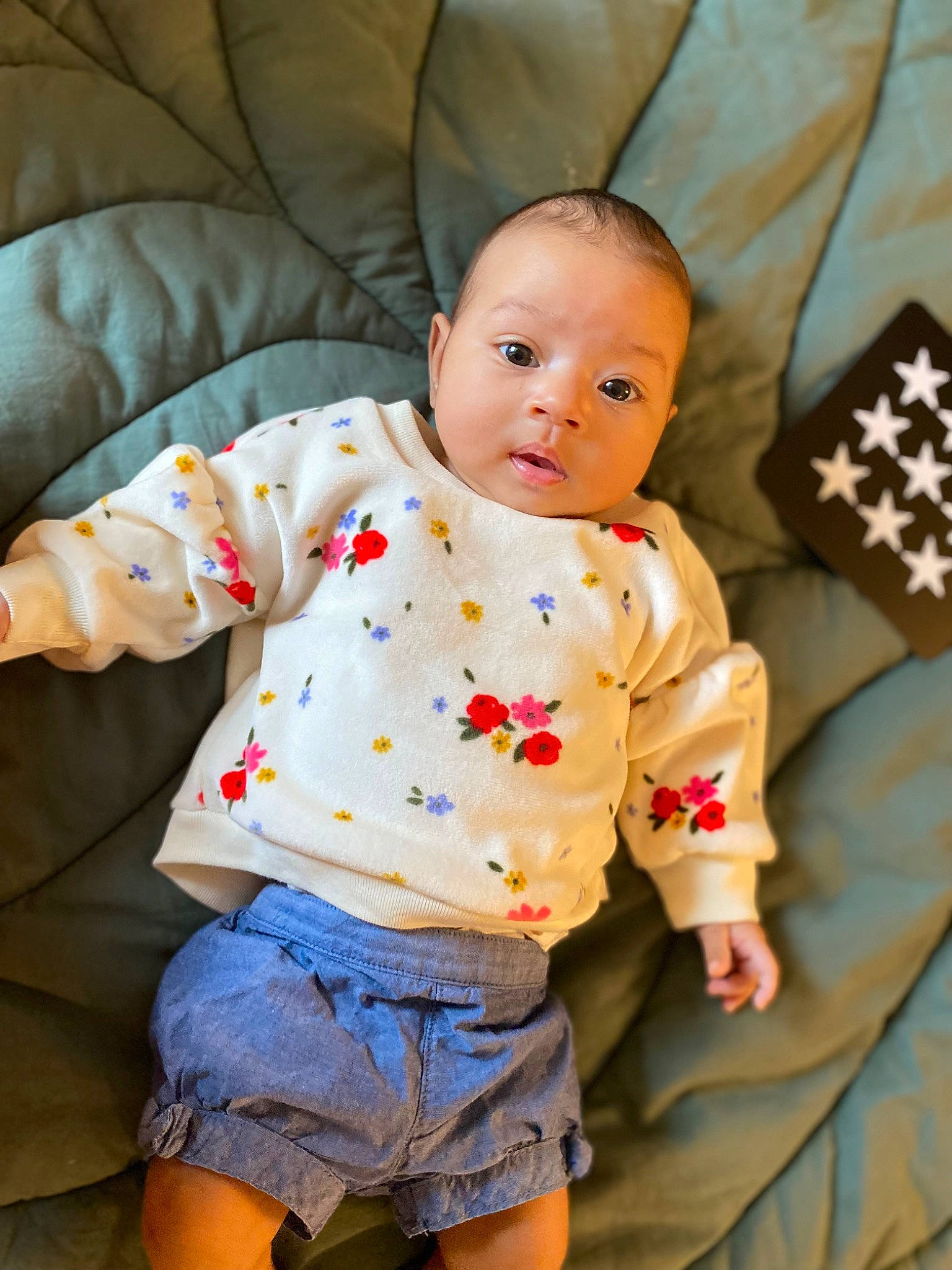 Esmé is registered to the contest to win money with this photo: baby, baby_toddler_clothing, cheek, child, comfort, couch, eye, face, happy, human_leg, linens, orange, person, shorts, sitting, skin, sleeve, textile, thigh, toddler