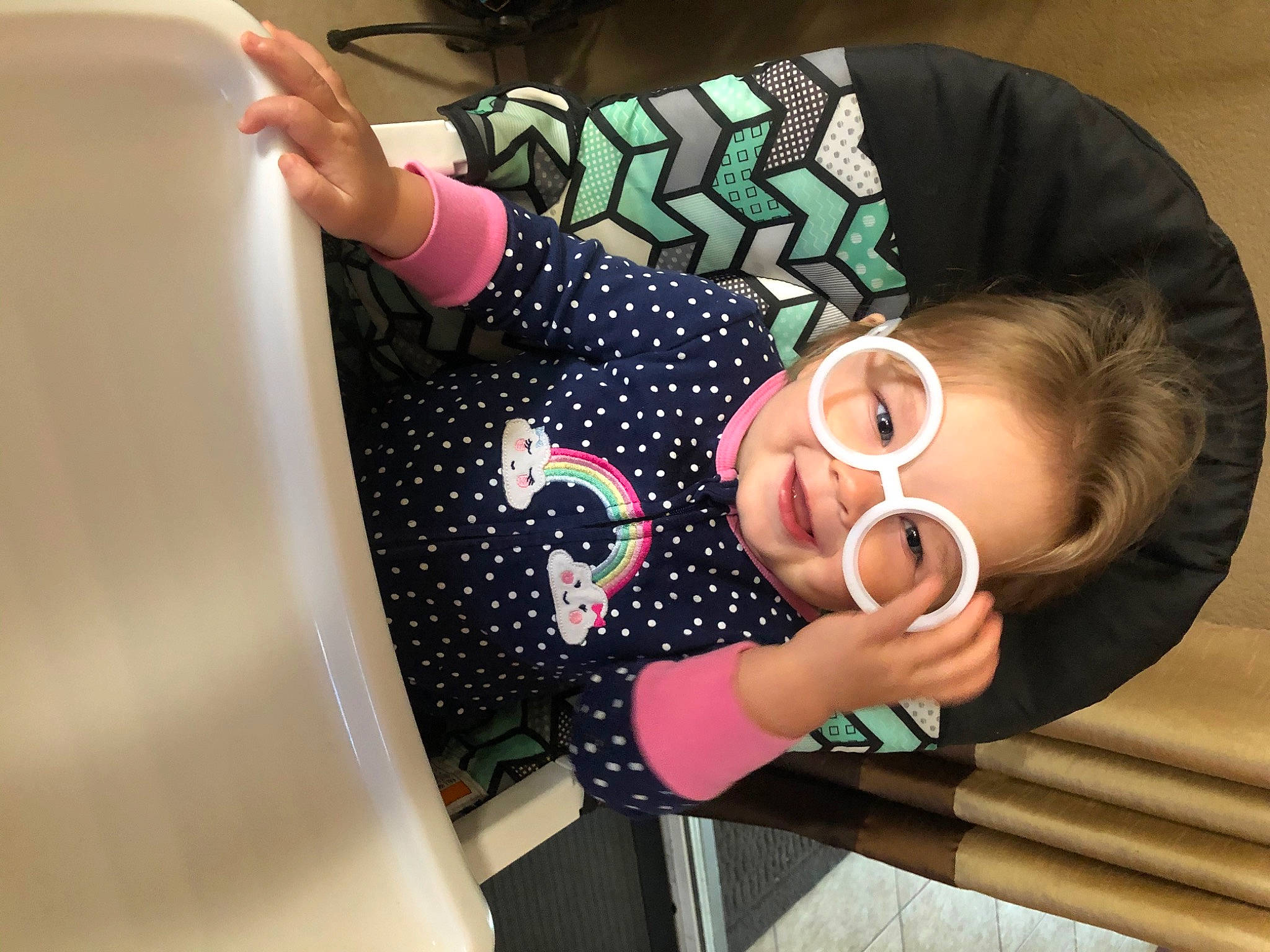 Saige is registered to the contest to win money with this photo: arm, baby_toddler_clothing, child, circle, eyewear, finger, fun, gesture, hand, happy, nail, neck, outerwear, pattern, person, sleeve, t_shirt, textile, thumb, toddler